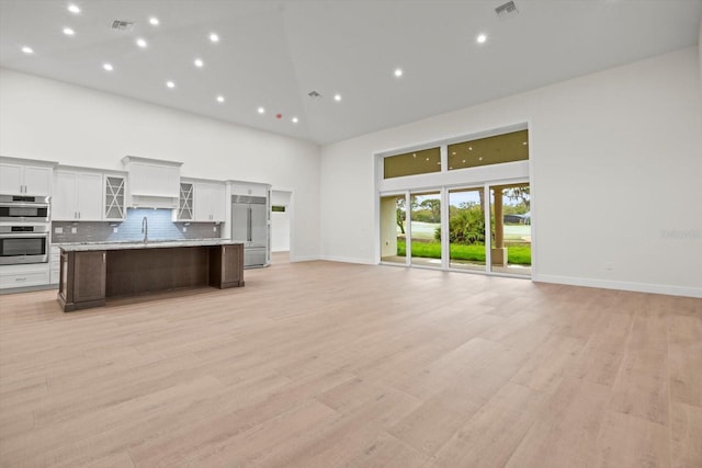 kitchen featuring appliances with stainless steel finishes, a large island with sink, light hardwood / wood-style floors, and high vaulted ceiling