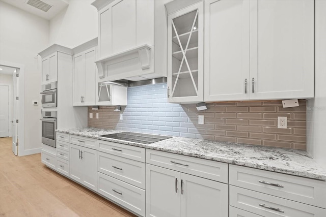 kitchen featuring decorative backsplash, white cabinetry, light stone countertops, light wood-type flooring, and black electric stovetop