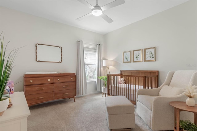 carpeted bedroom with a crib and ceiling fan