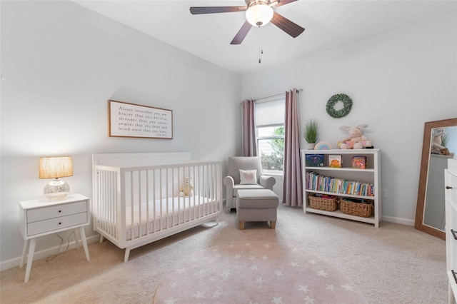 carpeted bedroom with a crib and ceiling fan