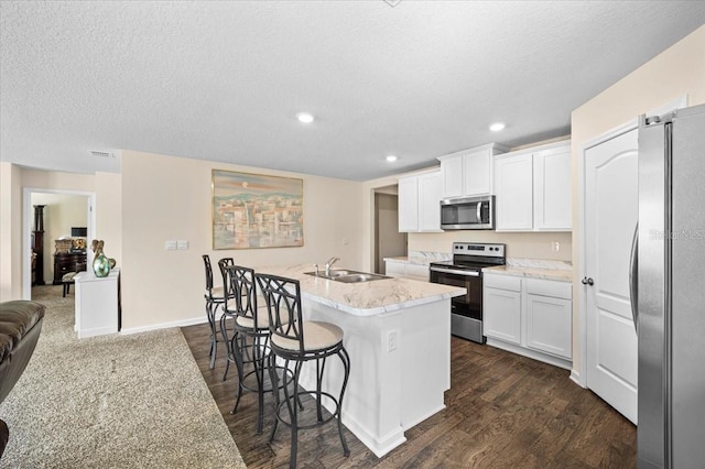 kitchen with dark hardwood / wood-style flooring, sink, stainless steel appliances, an island with sink, and white cabinets