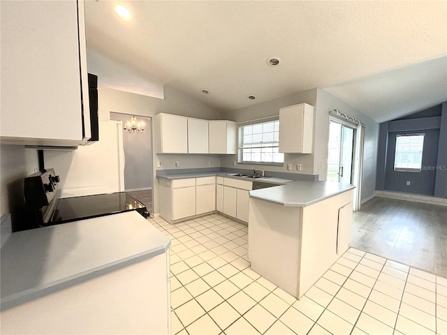 kitchen with lofted ceiling, kitchen peninsula, stove, white cabinetry, and light hardwood / wood-style floors