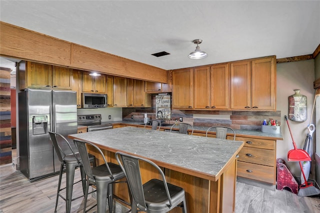 kitchen with a kitchen bar, a center island with sink, stainless steel appliances, and light wood-type flooring