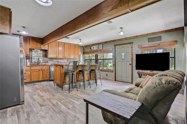 kitchen with backsplash, a breakfast bar, stainless steel appliances, beam ceiling, and light hardwood / wood-style flooring