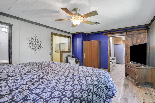 bedroom with ceiling fan, wooden walls, crown molding, a barn door, and light hardwood / wood-style flooring