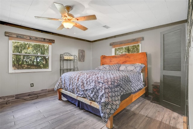 bedroom with hardwood / wood-style floors, ceiling fan, crown molding, and multiple windows