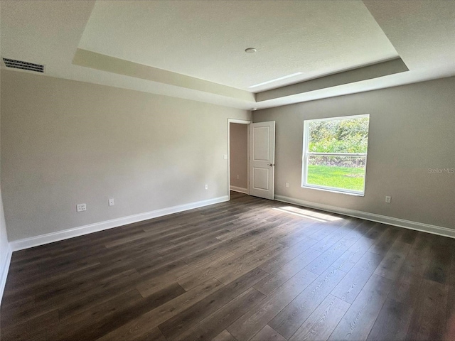 empty room featuring a raised ceiling and dark hardwood / wood-style flooring