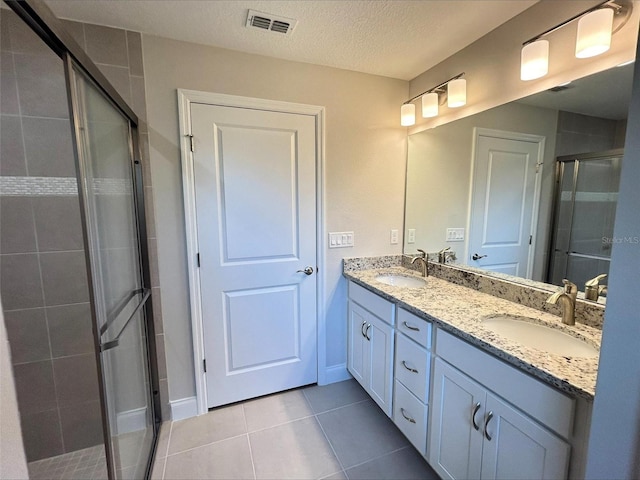 bathroom with tile patterned flooring, vanity, a shower with door, and a textured ceiling