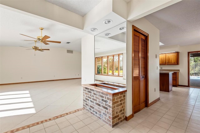 unfurnished living room featuring ceiling fan, light tile patterned floors, a textured ceiling, and vaulted ceiling