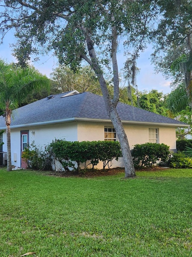 view of property exterior with central air condition unit, roof with shingles, a lawn, and stucco siding