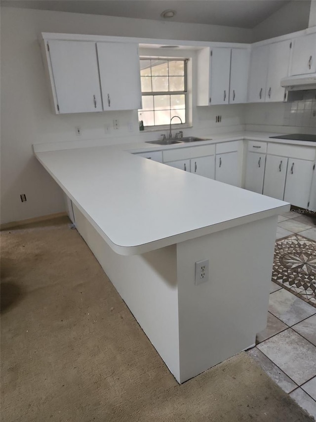 kitchen featuring a peninsula, under cabinet range hood, light countertops, and a sink