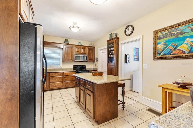 kitchen with a kitchen island, a kitchen breakfast bar, stainless steel appliances, light stone counters, and light tile patterned floors