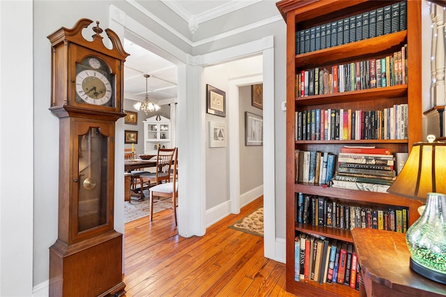 hallway featuring an inviting chandelier, ornamental molding, light wood-type flooring, and built in shelves