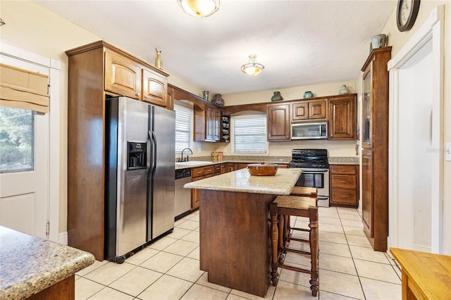 kitchen with light tile patterned floors, a kitchen breakfast bar, a kitchen island, sink, and stainless steel appliances