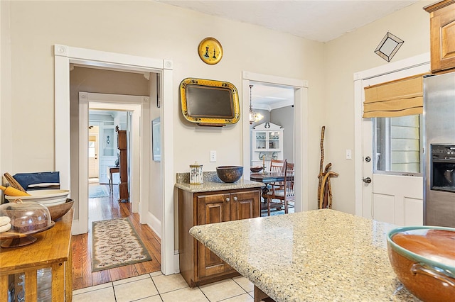 kitchen featuring crown molding, light stone countertops, light wood-type flooring, and stainless steel fridge