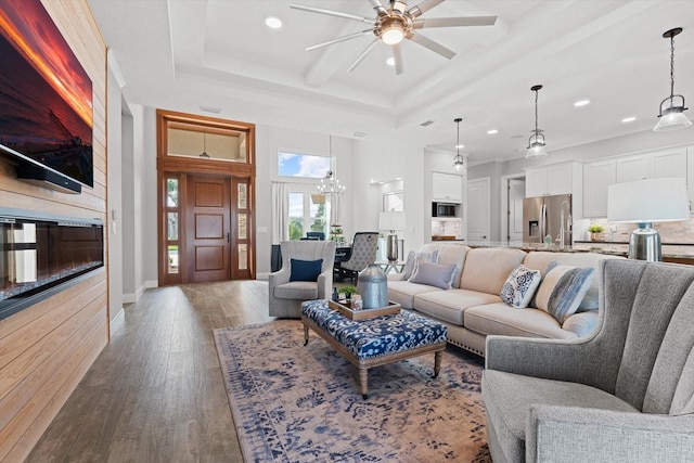 living room featuring hardwood / wood-style floors, a tray ceiling, and ceiling fan with notable chandelier