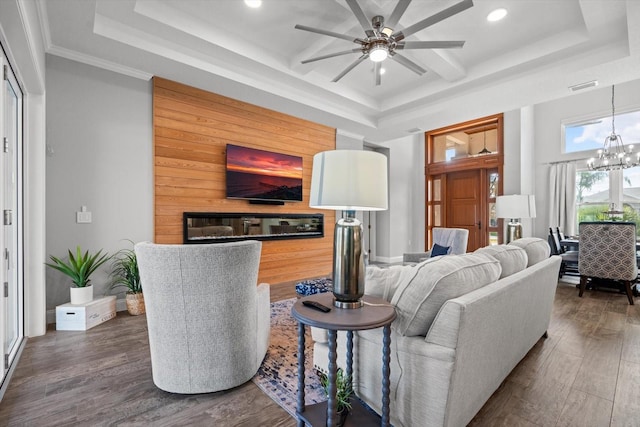 living room with ornamental molding, dark wood-type flooring, a tray ceiling, and ceiling fan with notable chandelier