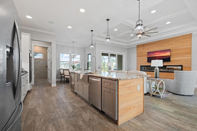 kitchen featuring light stone countertops, an island with sink, hanging light fixtures, stainless steel appliances, and dark wood-type flooring