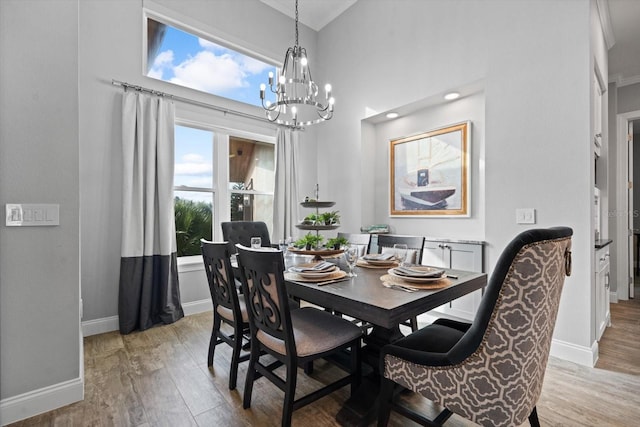 dining area with a towering ceiling, an inviting chandelier, and light wood-type flooring