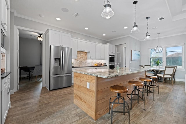 kitchen with hardwood / wood-style flooring, a large island, light stone countertops, white cabinetry, and appliances with stainless steel finishes