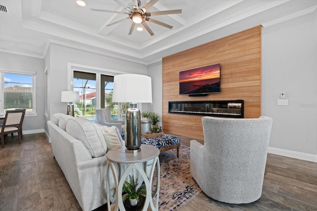 living room with ornamental molding, dark wood-type flooring, a tray ceiling, and ceiling fan