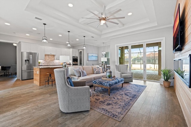 living room featuring crown molding, ceiling fan, light wood-type flooring, and a raised ceiling