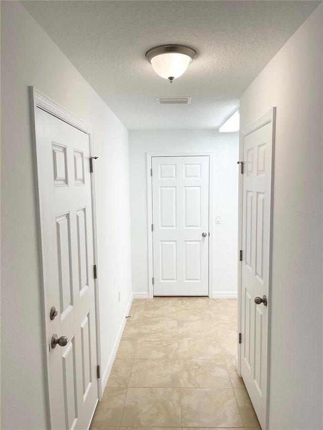 hall featuring a textured ceiling and light tile patterned floors