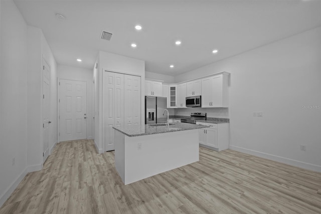 kitchen with stainless steel appliances, light hardwood / wood-style floors, light stone counters, white cabinets, and an island with sink