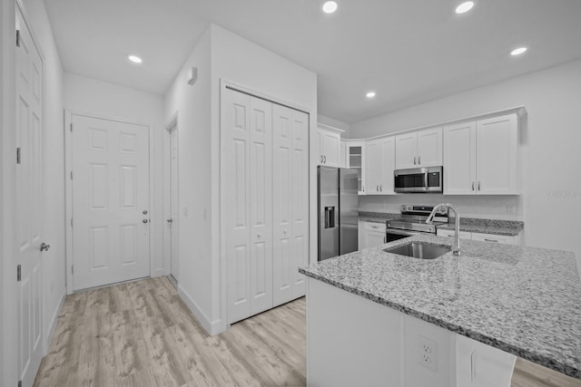 kitchen with light wood-type flooring, light stone countertops, appliances with stainless steel finishes, and white cabinets