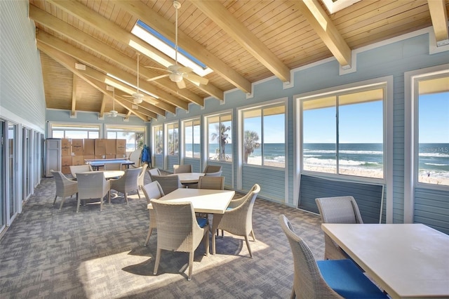 sunroom featuring a beach view, ceiling fan, vaulted ceiling with skylight, wooden ceiling, and a water view