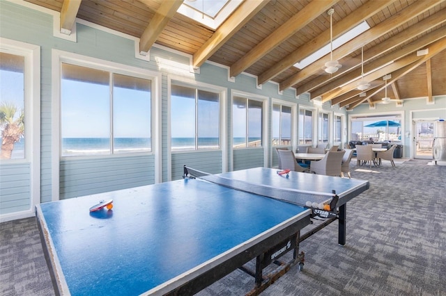 rec room featuring a water view, beamed ceiling, a skylight, and dark carpet