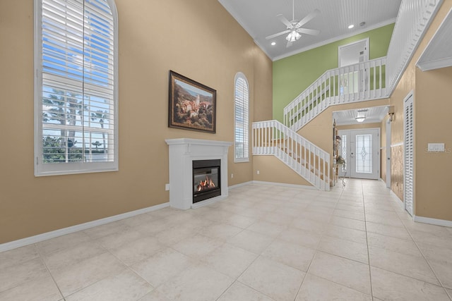 unfurnished living room featuring crown molding, light tile patterned flooring, a towering ceiling, and ceiling fan