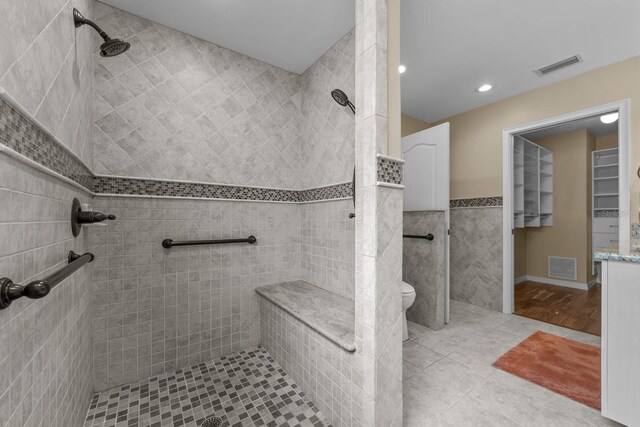 bathroom featuring toilet, vanity, tile walls, and tiled shower