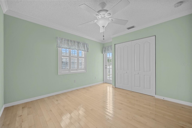 unfurnished bedroom featuring light wood-type flooring, a textured ceiling, a closet, ceiling fan, and crown molding