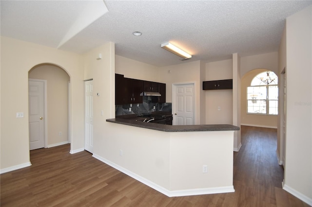 kitchen with dark wood-type flooring, dark brown cabinetry, kitchen peninsula, and a textured ceiling