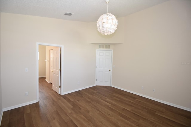 empty room featuring a textured ceiling, dark wood-type flooring, and a chandelier