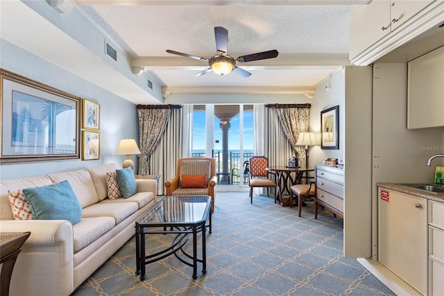 carpeted living room with sink, ceiling fan, beamed ceiling, and a textured ceiling