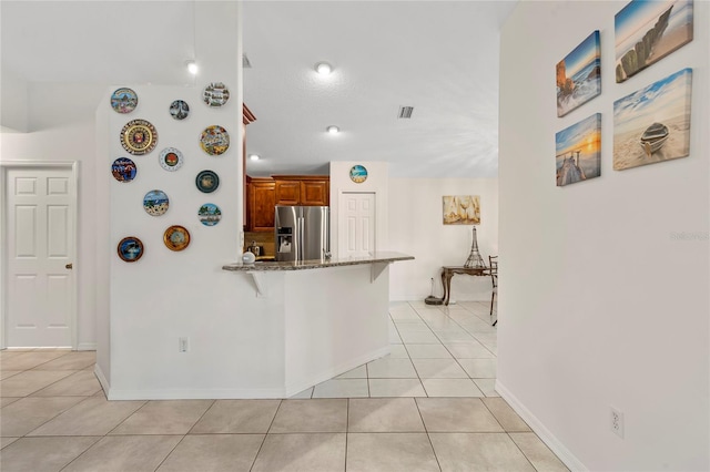 kitchen featuring stainless steel fridge with ice dispenser, light tile patterned floors, light stone countertops, a kitchen breakfast bar, and kitchen peninsula