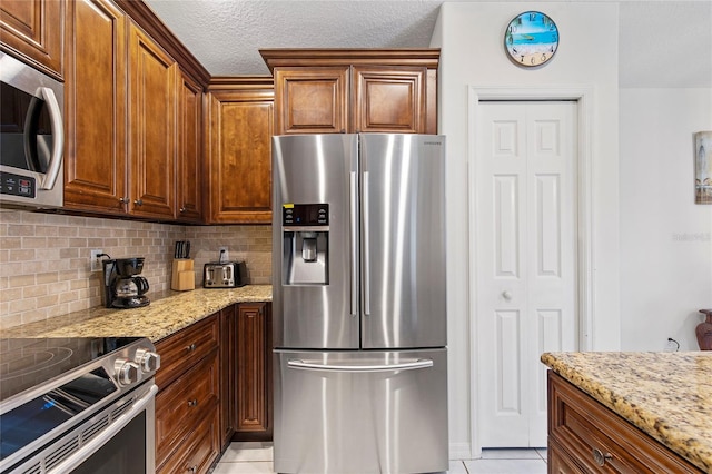 kitchen featuring stainless steel appliances, light tile patterned floors, backsplash, and light stone counters