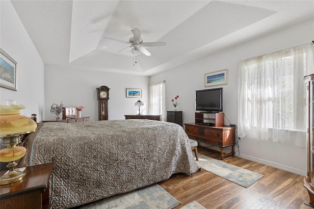 bedroom with ceiling fan, a textured ceiling, light wood-type flooring, and a tray ceiling