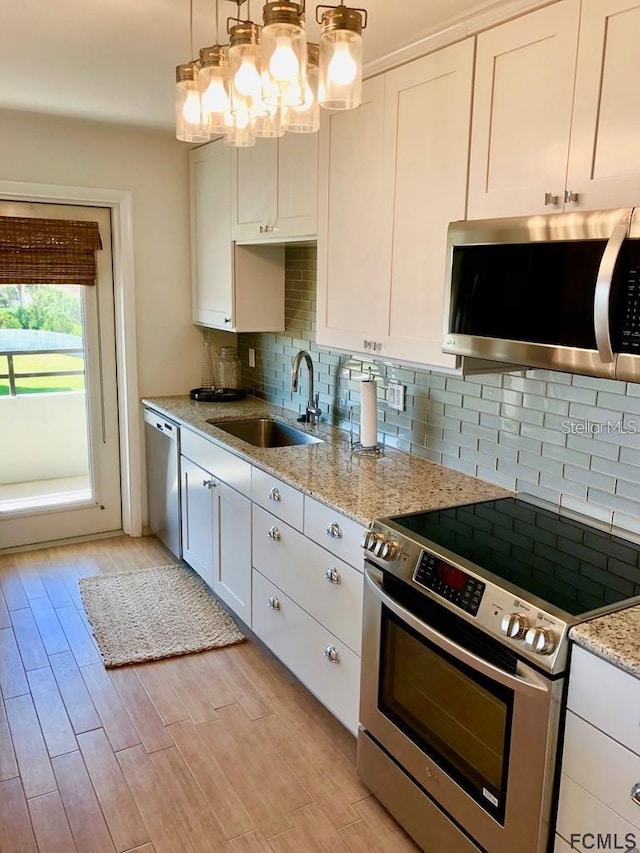 kitchen with sink, white cabinets, decorative light fixtures, and stainless steel appliances