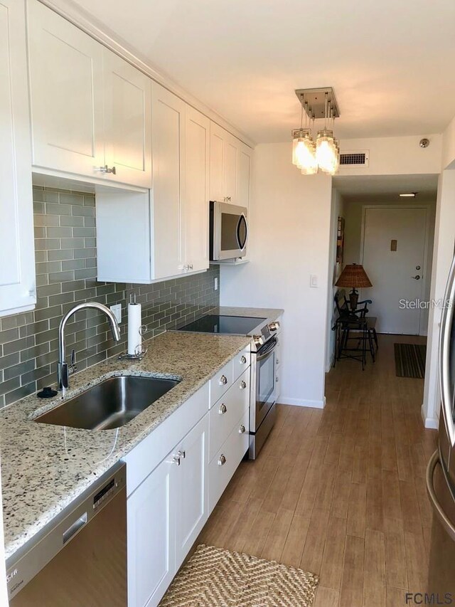 kitchen featuring sink, light wood-type flooring, white cabinetry, stainless steel appliances, and pendant lighting