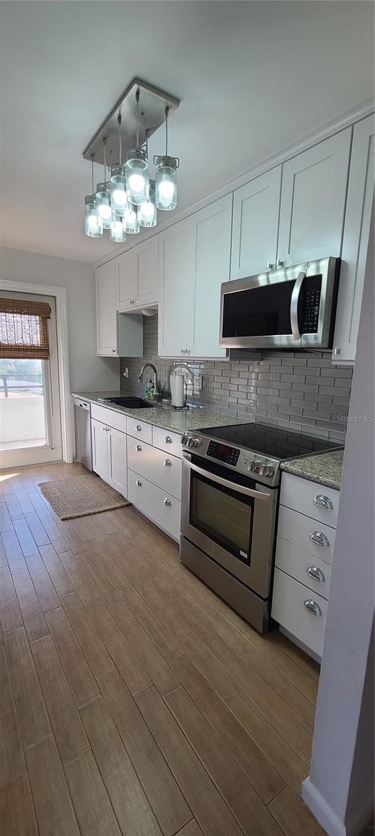 kitchen featuring stainless steel appliances, sink, decorative light fixtures, white cabinets, and light hardwood / wood-style floors