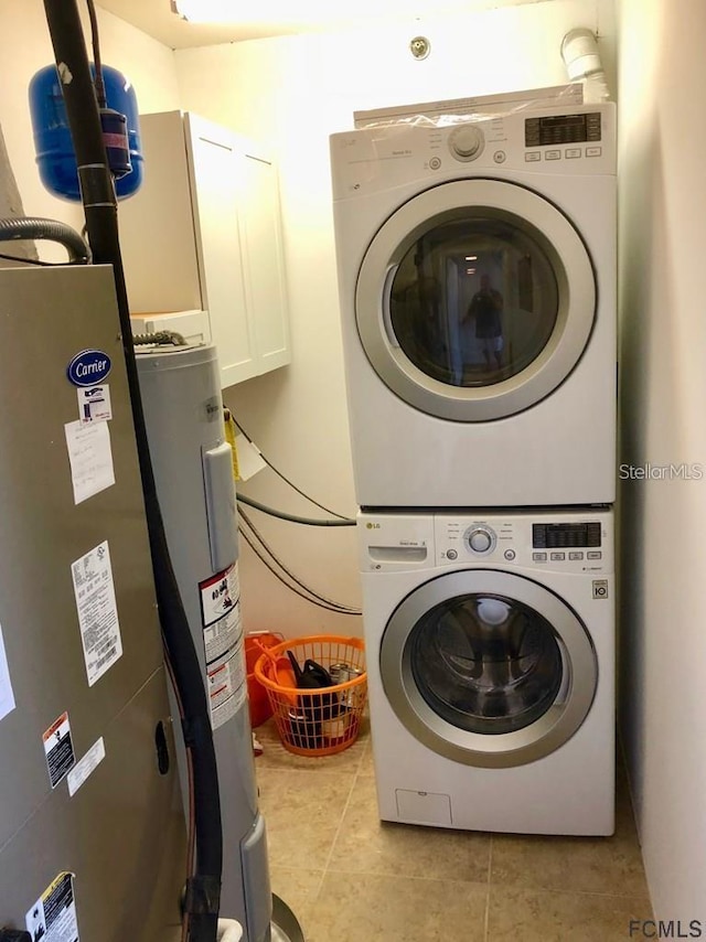 clothes washing area featuring stacked washing maching and dryer, electric water heater, and light tile patterned flooring