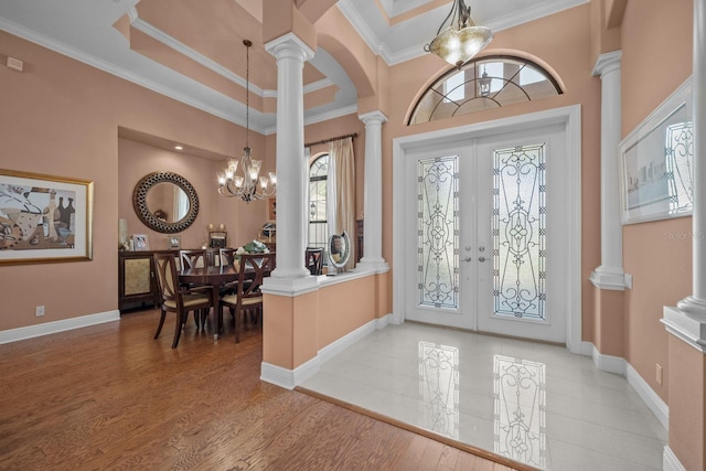 foyer entrance with ornate columns, french doors, hardwood / wood-style floors, a chandelier, and ornamental molding