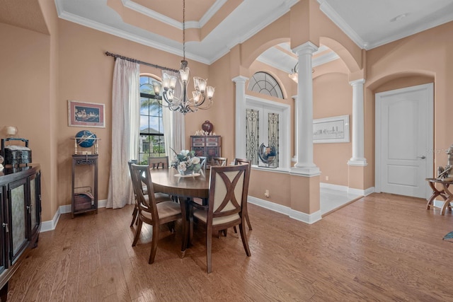 dining space with french doors, crown molding, hardwood / wood-style flooring, a notable chandelier, and decorative columns