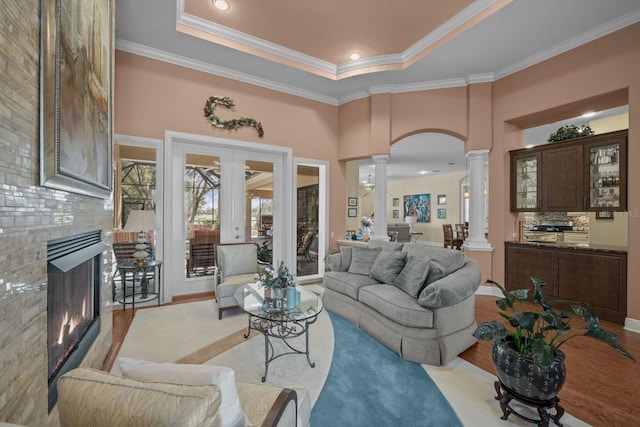 living room featuring decorative columns, french doors, ornamental molding, light hardwood / wood-style floors, and a tiled fireplace