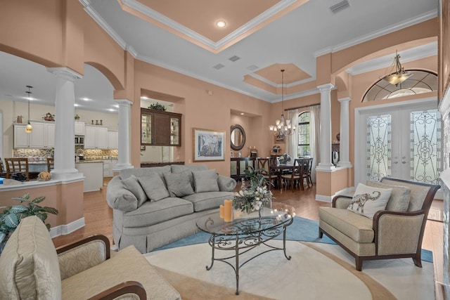 living room with french doors, an inviting chandelier, light hardwood / wood-style floors, a tray ceiling, and ornamental molding