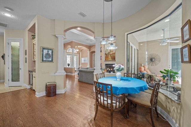 dining area featuring crown molding, ceiling fan, ornate columns, a large fireplace, and wood-type flooring