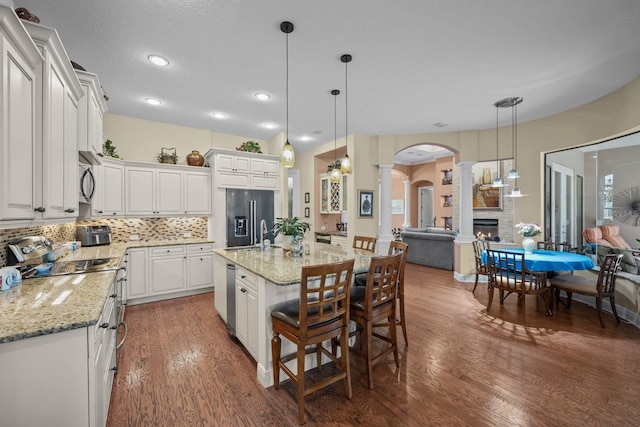 kitchen featuring hanging light fixtures, dark hardwood / wood-style flooring, decorative columns, an island with sink, and appliances with stainless steel finishes